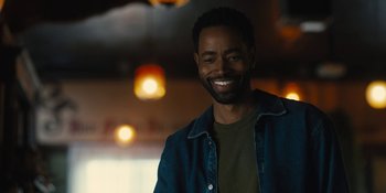 Movie still from “Somebody I Used to Know” (2023), directed by Dave Franco – A man smiling for the camera in front of lights; Close Up shot, Over the shoulder angle