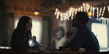Movie still from “Somebody I Used to Know” (2023), directed by Dave Franco – A man and a woman sitting at a table with a bottle of beer; Medium shot, Over the shoulder angle