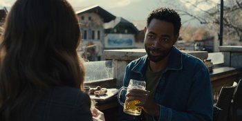 Movie still from “Somebody I Used to Know” (2023), directed by Dave Franco – A man holding a glass of beer while sitting at a table with a woman; Medium shot, Over the shoulder angle