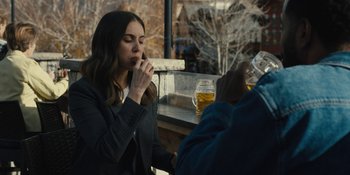 Movie still from “Somebody I Used to Know” (2023), directed by Dave Franco – A woman sitting at an outdoor table with a glass of beer; Medium shot, Over the shoulder angle