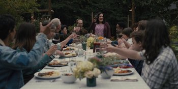 Movie still from “Somebody I Used to Know” (2023), directed by Dave Franco – A group of people sitting at a table with plates of food; Wide shot, Over the shoulder angle