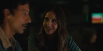 Movie still from “Somebody I Used to Know” (2023), directed by Dave Franco – A woman smiles at the camera while sitting in a dark room; Close Up shot, Over the shoulder angle