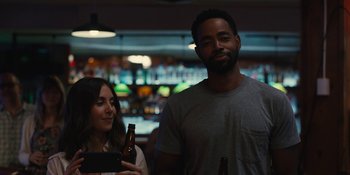 Movie still from “Somebody I Used to Know” (2023), directed by Dave Franco – A man and a woman standing next to each other holding beer bottles; Medium shot, Over the shoulder angle