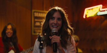 Movie still from “Somebody I Used to Know” (2023), directed by Dave Franco – A woman holding a microphone and smiling for the camera; Close Up shot, Over the shoulder angle