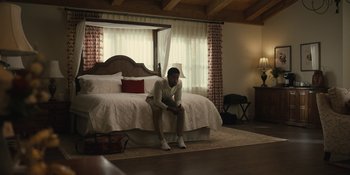 Movie still from “Somebody I Used to Know” (2023), directed by Dave Franco – A man sitting on the edge of a bed in front of a large bed; Wide shot, High angle