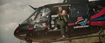 Movie still from “Son of a Gun” (2014), directed by Julius Avery – A man sitting in the door of a black helicopter; Wide shot, Low angle