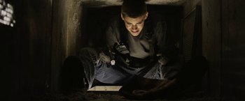 Movie still from “Son of a Gun” (2014), directed by Julius Avery – A man sitting on the ground looking at a piece of paper; Medium shot, Low angle