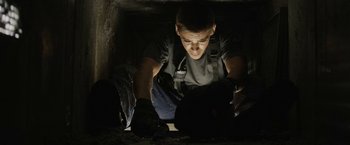 Movie still from “Son of a Gun” (2014), directed by Julius Avery – A man is looking down at something in the dark; Medium shot, Low angle