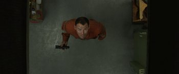 Movie still from “Son of a Gun” (2014), directed by Julius Avery – A man holding a cell phone while standing in a room; Medium shot, Overhead angle