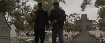 Movie still from “Son of a Gun” (2014), directed by Julius Avery – Two men standing next to each other in a cemetery; Medium shot, Over the shoulder angle