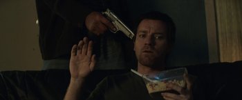 Movie still from “Son of a Gun” (2014), directed by Julius Avery – A man holding a gun in front of another man holding food; Medium shot, Overhead angle