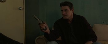 Movie still from “Son of a Gun” (2014), directed by Julius Avery – A man holding a gun while sitting on a chair; Medium shot, Low angle