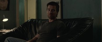 Movie still from “Son of a Gun” (2014), directed by Julius Avery – A man sitting on top of a black leather couch; Close Up shot, Over the shoulder angle