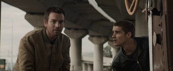 Movie still from “Son of a Gun” (2014), directed by Julius Avery – Two men standing next to each other under a bridge; Medium shot, Low angle