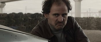 Movie still from “Son of a Gun” (2014), directed by Julius Avery – A person wearing a brown jacket; Close Up shot, Low angle