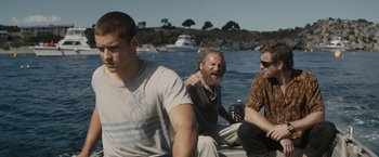 Movie still from “Son of a Gun” (2014), directed by Julius Avery – A group of people sitting on a boat in the water; Medium shot, Over the shoulder angle