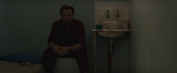Movie still from “Son of a Gun” (2014), directed by Julius Avery – A man sitting on top of a toilet in front of a sink; Medium shot, Over the shoulder angle