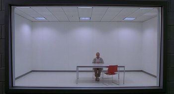 Movie still from “One Hour Photo” (2002), directed by Mark Romanek – A man sitting at a table in front of a red chair; Wide shot, Low angle
