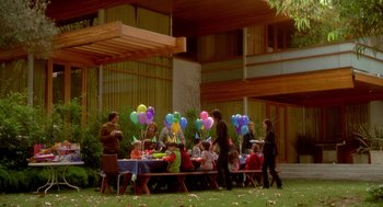 Movie still from “One Hour Photo” (2002), directed by Mark Romanek – A group of people standing around a table with balloons; Extreme Wide shot, High angle