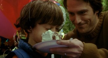Movie still from “One Hour Photo” (2002), directed by Mark Romanek – A man and a boy are eating a cake together; Close Up shot, Over the shoulder angle