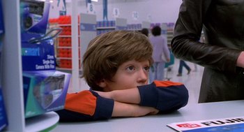 Movie still from “One Hour Photo” (2002), directed by Mark Romanek – A young boy sitting at a table in a store; Medium shot, Over the shoulder angle