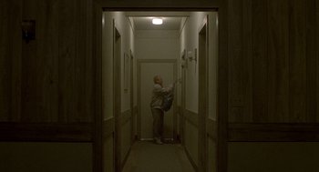 Movie still from “One Hour Photo” (2002), directed by Mark Romanek – A man standing in a hallway holding a guitar; Wide shot, Low angle