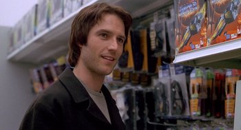 Movie still from “One Hour Photo” (2002), directed by Mark Romanek – A man standing in front of a wall with many items on it; Close Up shot, Over the shoulder angle