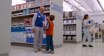 Movie still from “One Hour Photo” (2002), directed by Mark Romanek – A man and a boy are talking in a store; Wide shot, Over the shoulder angle