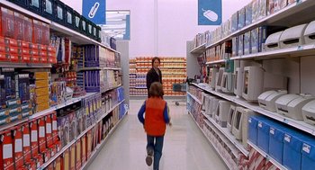Movie still from “One Hour Photo” (2002), directed by Mark Romanek – A woman and a child walking down a aisle in a grocery store; Wide shot, Over the shoulder angle