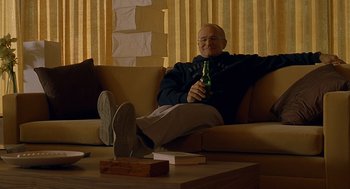 Movie still from “One Hour Photo” (2002), directed by Mark Romanek – A man sitting on a couch holding a bottle of beer; Medium shot, Low angle
