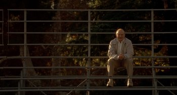 Movie still from “One Hour Photo” (2002), directed by Mark Romanek – An older man sitting on a metal railing; Wide shot, Low angle