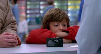 Movie still from “One Hour Photo” (2002), directed by Mark Romanek – A little boy sitting at a table with his arms crossed; Close Up shot, Over the shoulder angle