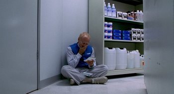 Movie still from “One Hour Photo” (2002), directed by Mark Romanek – A man sitting on the ground looking at a cell phone; Wide shot, High angle