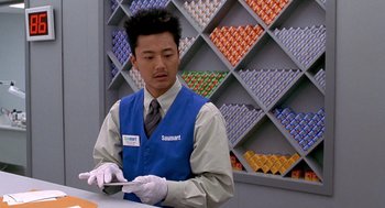 Movie still from “One Hour Photo” (2002), directed by Mark Romanek – A man in a blue vest and white gloves is working; Medium shot, Over the shoulder angle