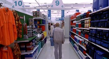Movie still from “One Hour Photo” (2002), directed by Mark Romanek – A man walking down a aisle in a store; Wide shot, High angle