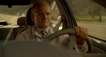 Movie still from “One Hour Photo” (2002), directed by Mark Romanek – An older man driving a car in a suit and tie; Close Up shot, Low angle