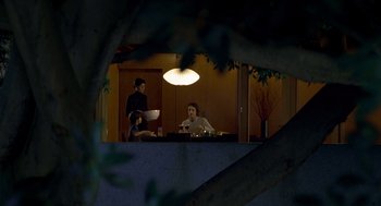 Movie still from “One Hour Photo” (2002), directed by Mark Romanek – A group of people sitting at a table in the dark; Wide shot, High angle