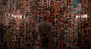 Movie still from “One Hour Photo” (2002), directed by Mark Romanek – A man standing in front of a wall covered in pictures; Extreme Wide shot, Overhead angle
