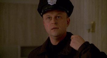 Movie still from “One Hour Photo” (2002), directed by Mark Romanek – A man in a police officer's uniform with his fist raised; Close Up shot, Low angle