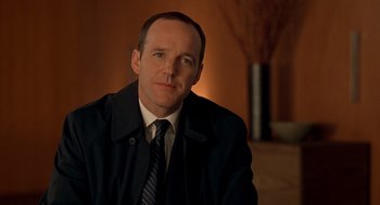 Movie still from “One Hour Photo” (2002), directed by Mark Romanek – A man wearing a suit and tie sitting in front of a wall; Close Up shot, Over the shoulder angle