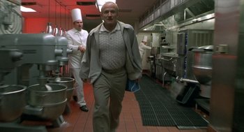 Movie still from “One Hour Photo” (2002), directed by Mark Romanek – A man walking in a kitchen wearing a chef's hat; Medium shot, Low angle