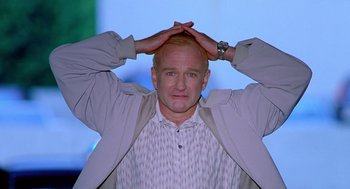 Movie still from “One Hour Photo” (2002), directed by Mark Romanek – A man in a white shirt and a white jacket is holding his hands to his head; Close Up shot, Low angle