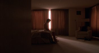 Movie still from “One Hour Photo” (2002), directed by Mark Romanek – A person sitting on a bed in a room; Wide shot, Low angle
