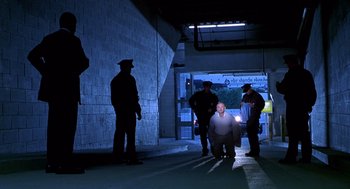 Movie still from “One Hour Photo” (2002), directed by Mark Romanek – A man kneeling down in front of a group of police officers; Wide shot, Low angle