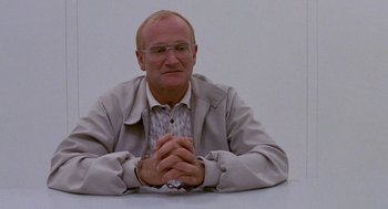 Movie still from “One Hour Photo” (2002), directed by Mark Romanek – An older man sitting at a table in front of a white wall; Medium shot, Low angle