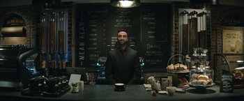 Movie still from “Sonic the Hedgehog 2” (2022), directed by Jeff Fowler – A man standing at a table with a cup of coffee; Wide shot, Low angle