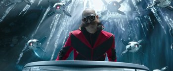 Movie still from “Sonic the Hedgehog 2” (2022), directed by Jeff Fowler – A man in a red and black jacket and goggles; Medium shot, Low angle