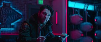 Movie still from “Sonic the Hedgehog 2” (2022), directed by Jeff Fowler – A man holding a plate of food in a dark room; Medium shot, Over the shoulder angle