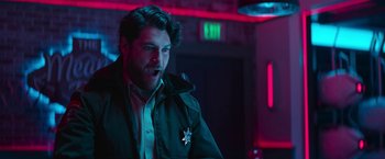 Movie still from “Sonic the Hedgehog 2” (2022), directed by Jeff Fowler – A man in a green jacket is standing in front of a neon sign; Medium shot, Over the shoulder angle