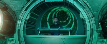 Movie still from “Sonic the Hedgehog 2” (2022), directed by Jeff Fowler – A man sitting at a desk in a room with a green background; Medium shot, Low angle